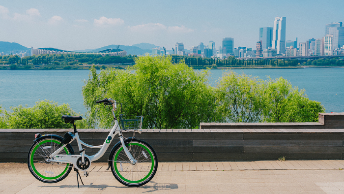 Green Seoul on-demand rental bicycle standing against the fence, Han river as background
